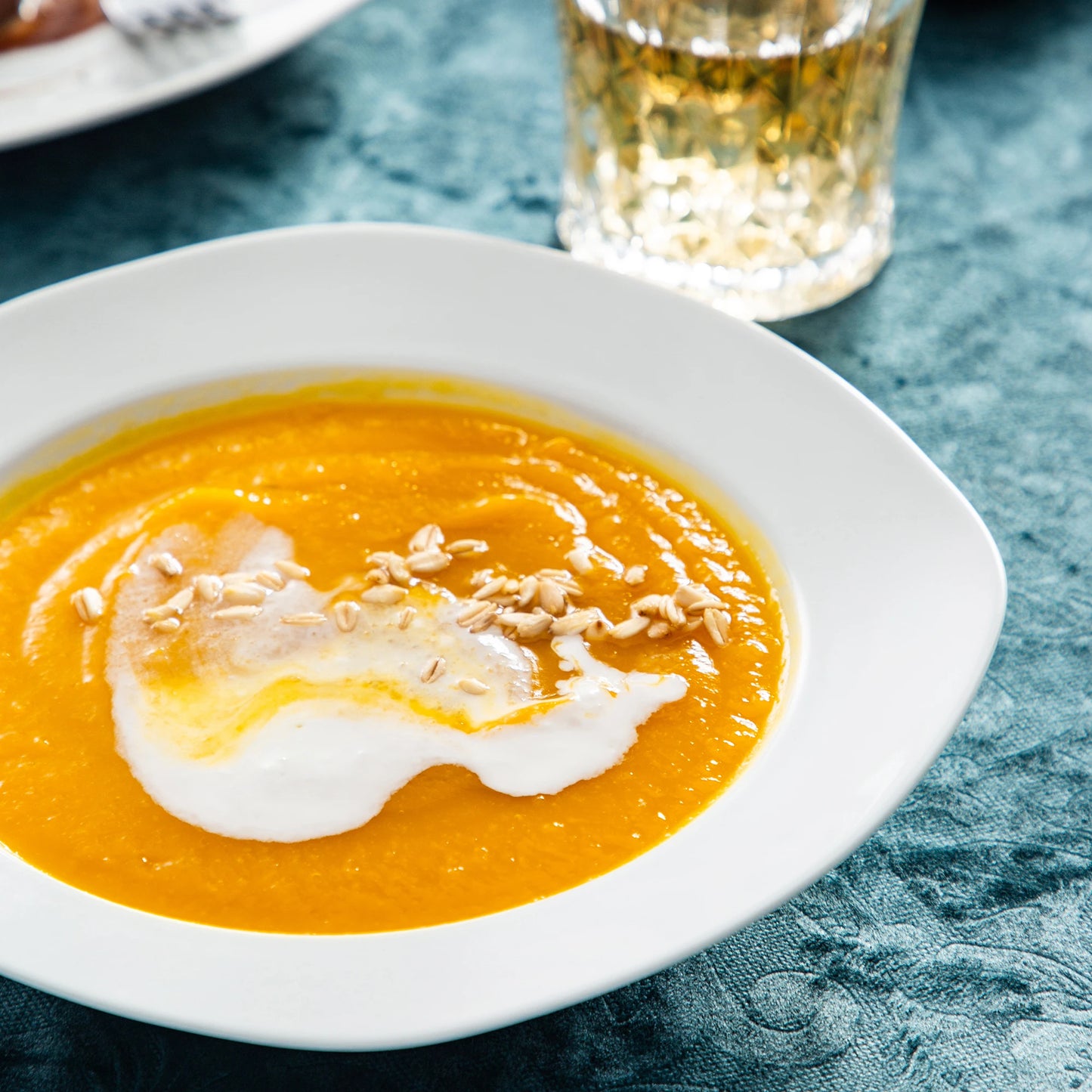 Orange soup with a poached egg on a white plate, served on a textured blue tablecloth.