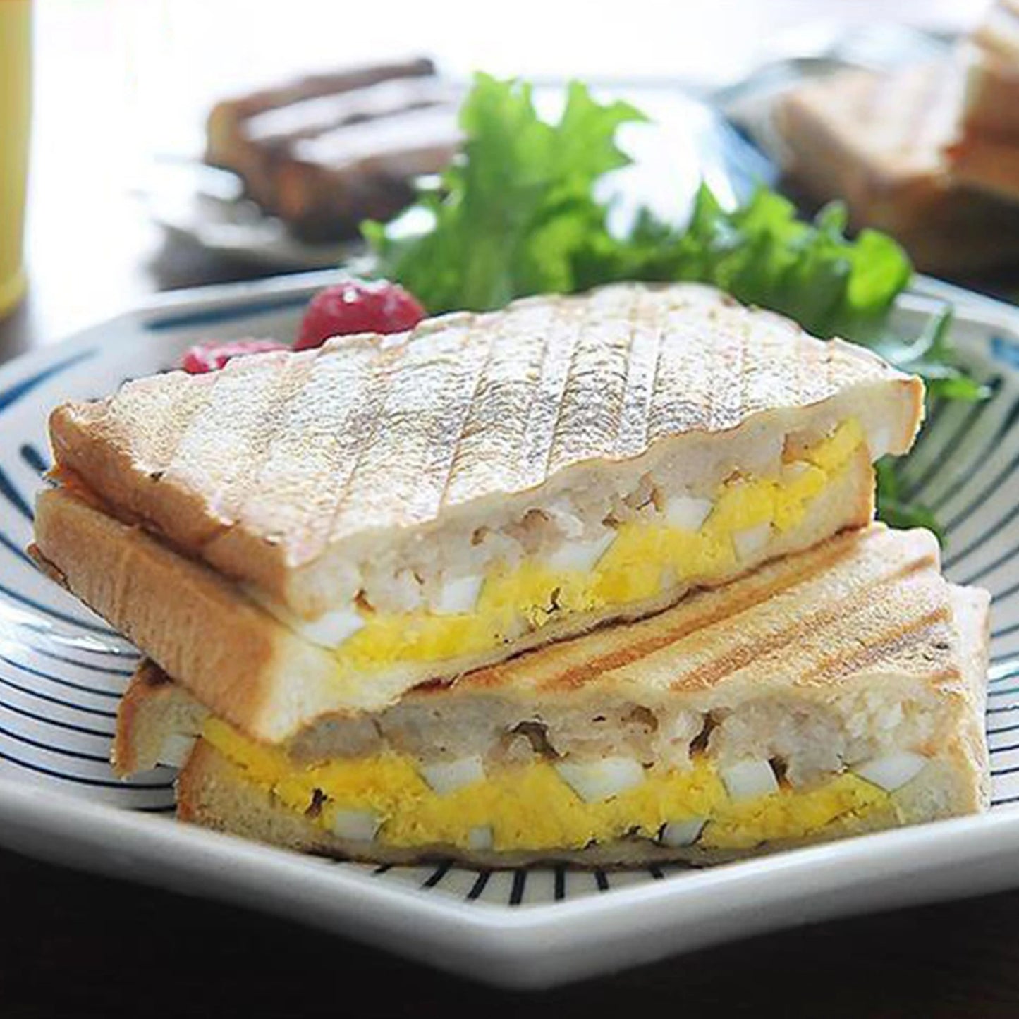 Grilled cheese sandwich with egg and tomato on a white plate with a blue rim.