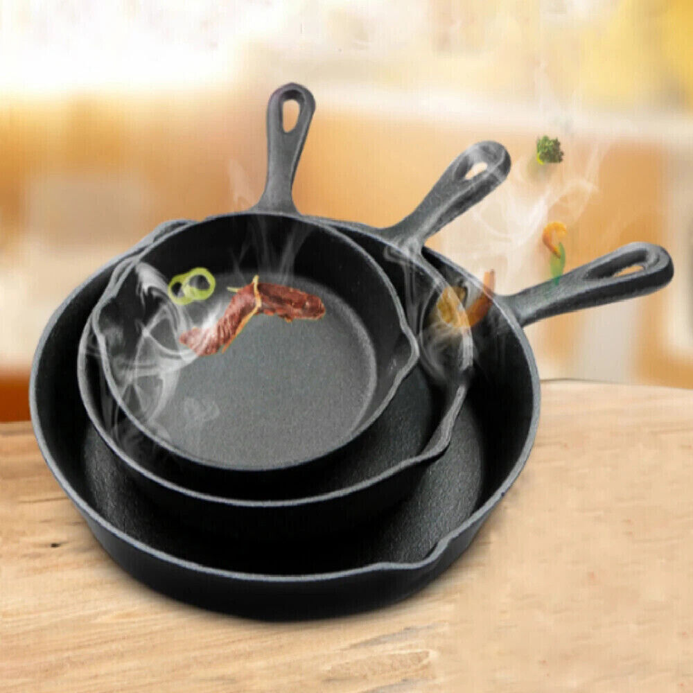 Set of three black cast iron skillets on a wooden surface with a blurred kitchen background.