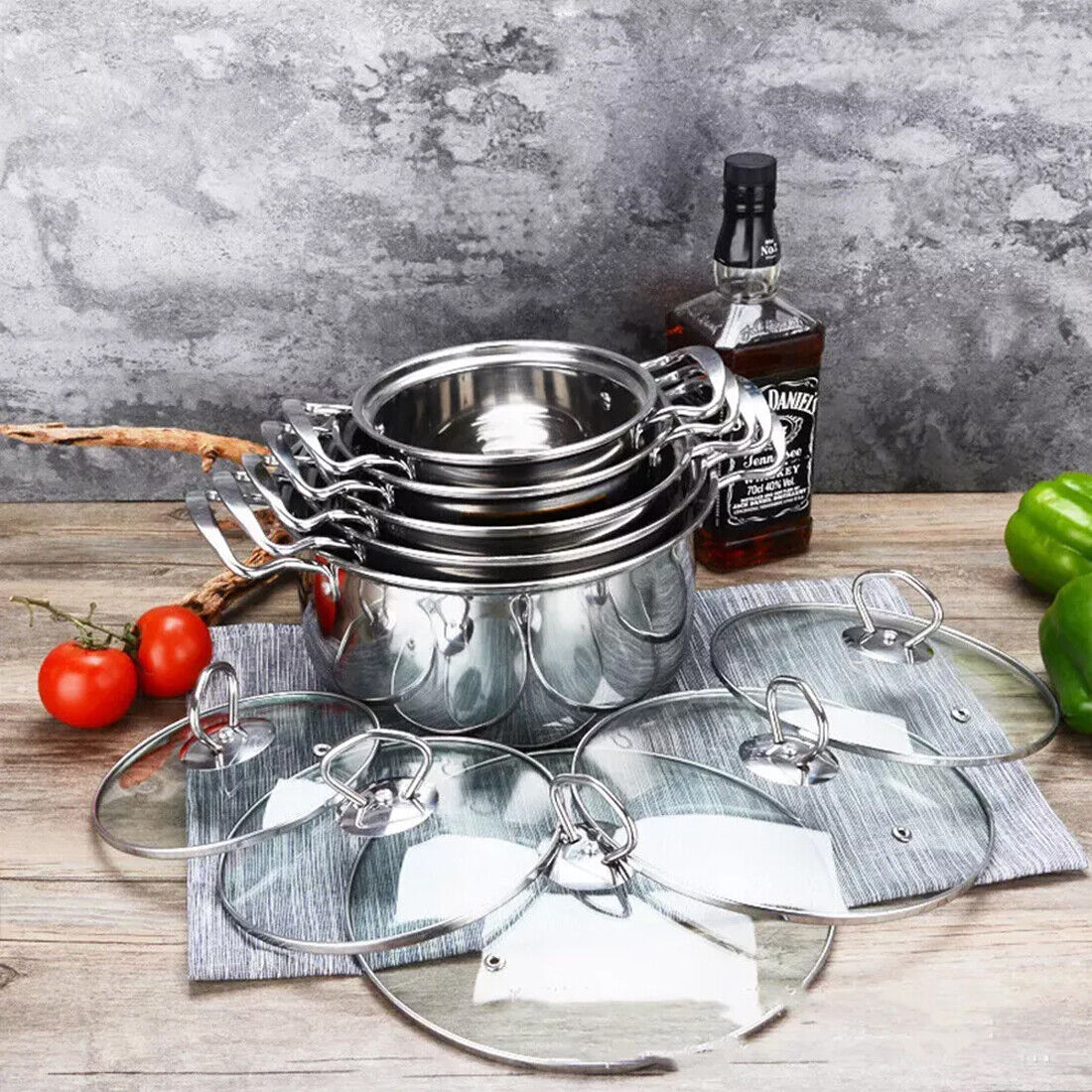 Set of metal cookware with glass lids on a wooden surface with a bottle of Jack Daniel's whiskey.