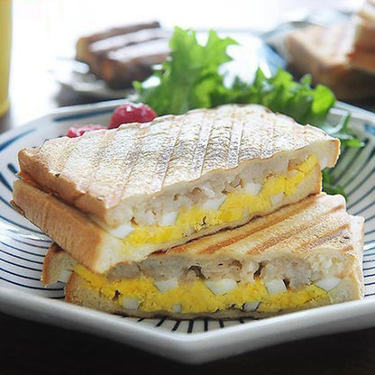 Grilled cheese sandwich with egg and tomato on a white plate with a blue rim.