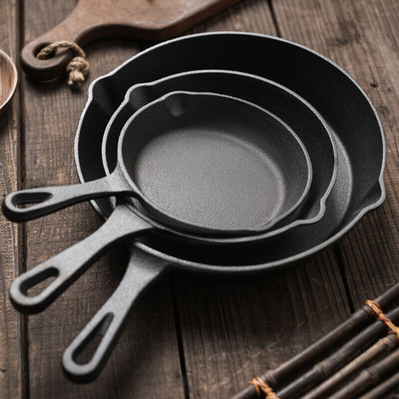 Set of three black cast iron skillets on a wooden surface
