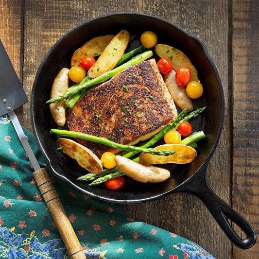 Fried fish with vegetables in a cast iron skillet on a wooden surface